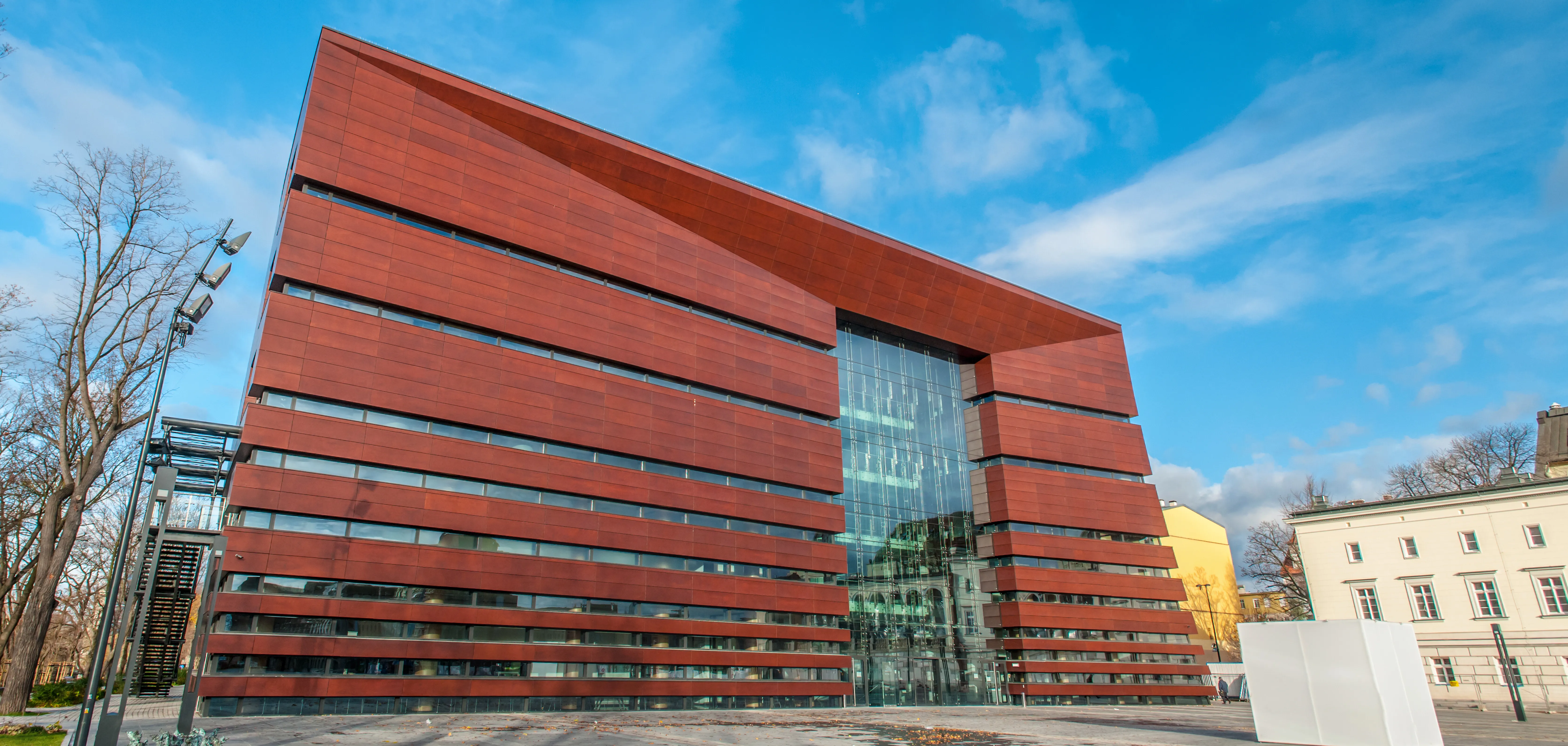 Szeroka panorama czerwono-brązowej fasady Narodowego Forum Muzyki od strony placu Wolności.